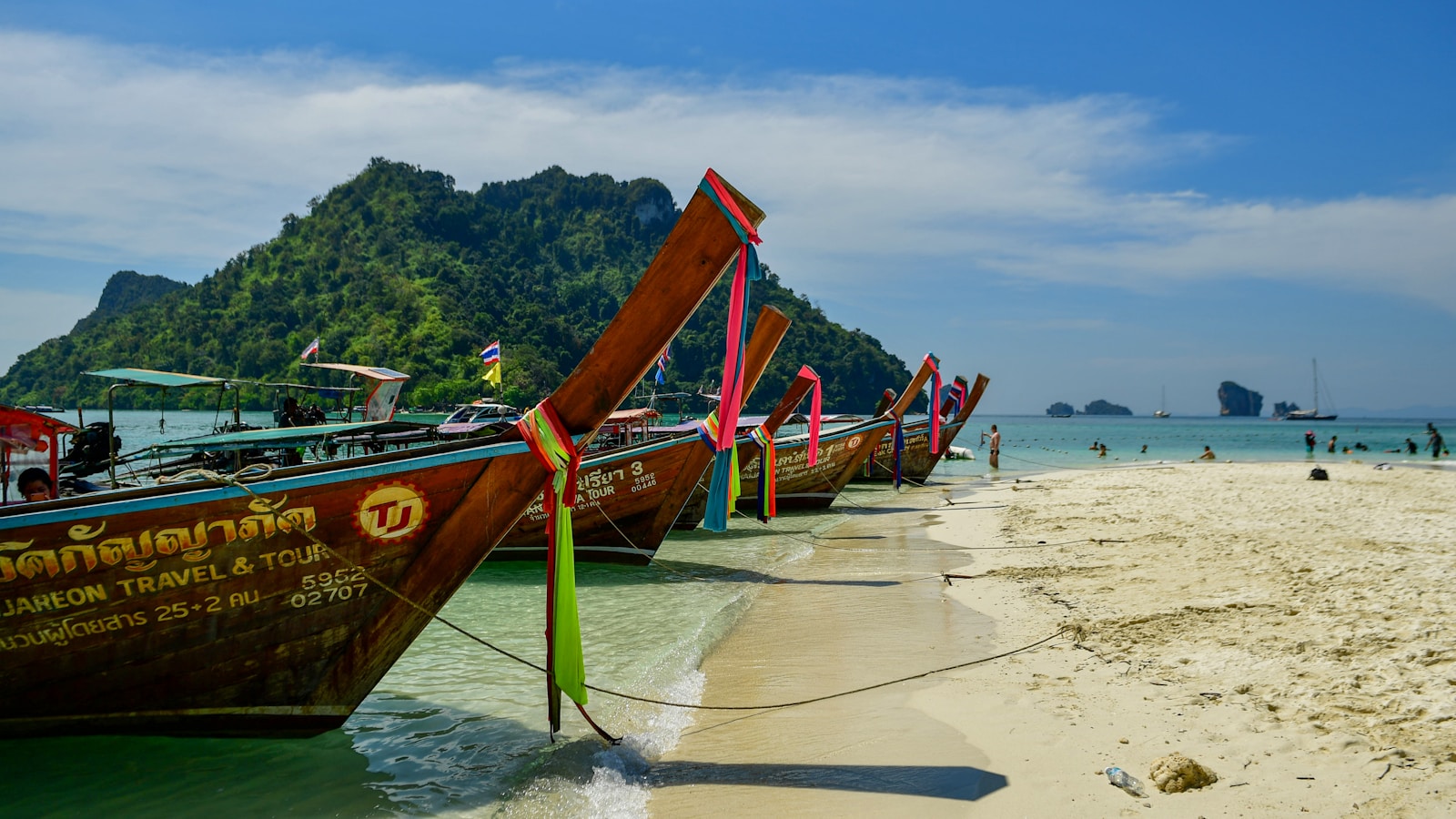 Long-tail boats on a white-sand beach below a limestone island, Koh Lanta